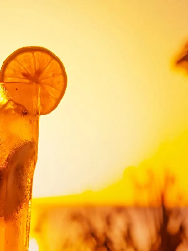 Un cocktail au coucher du soleil sous un parasol en paille à Eden Beach