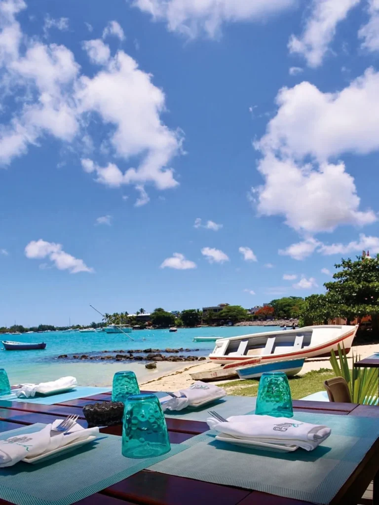 Tables dressées en bord de plage à Eden Beach, avec le lagon et les pirogues en arrière-plan